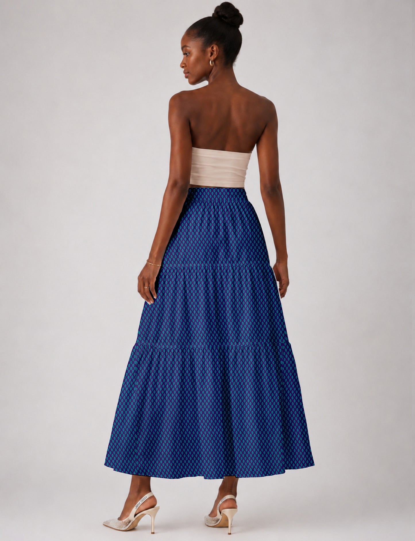 Woman wearing a blue midi tiered skirt with a small geometric pattern, shown from the back, paired with beige heels