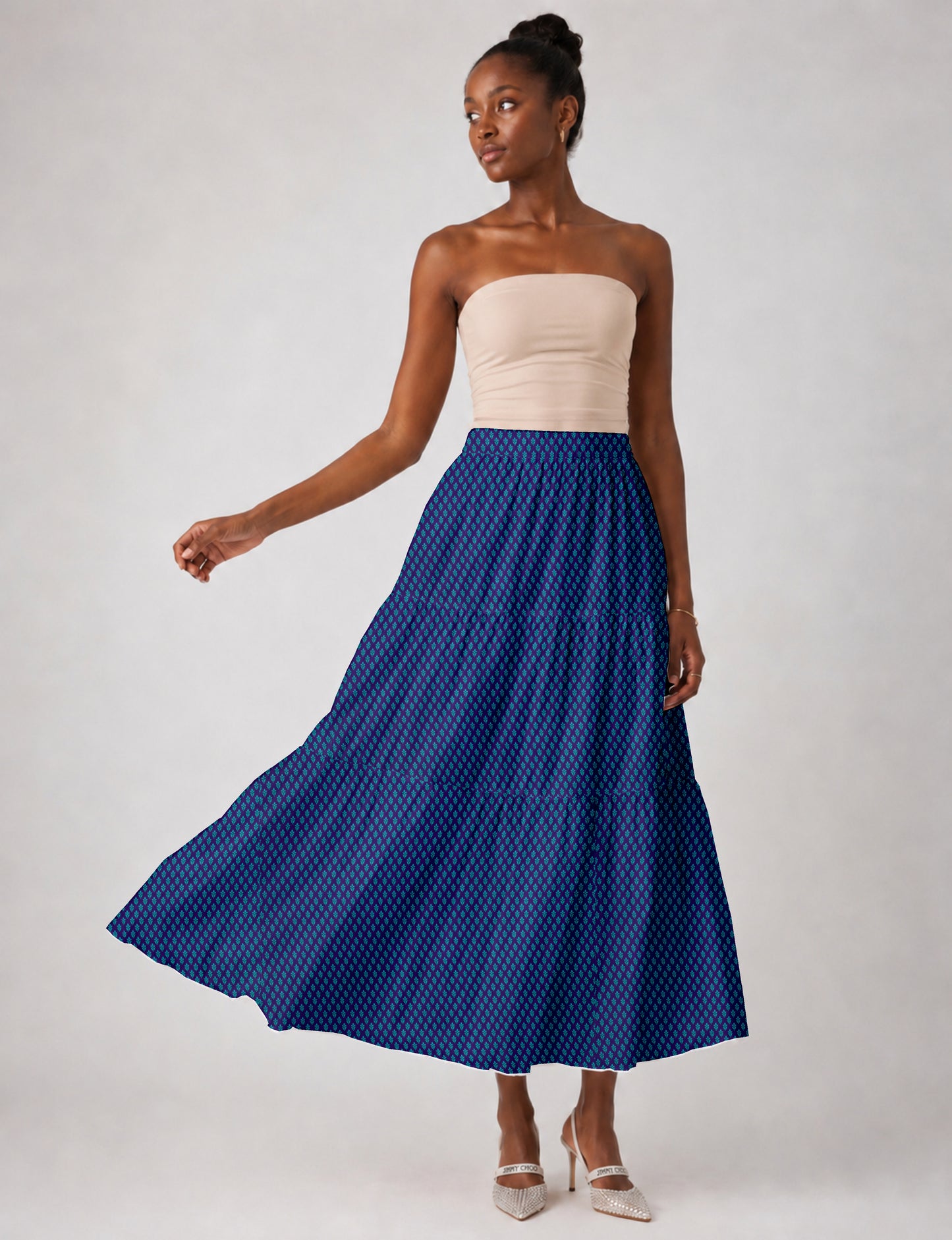 Woman wearing a blue midi tiered skirt with a small geometric pattern, paired with a beige strapless top and white heels