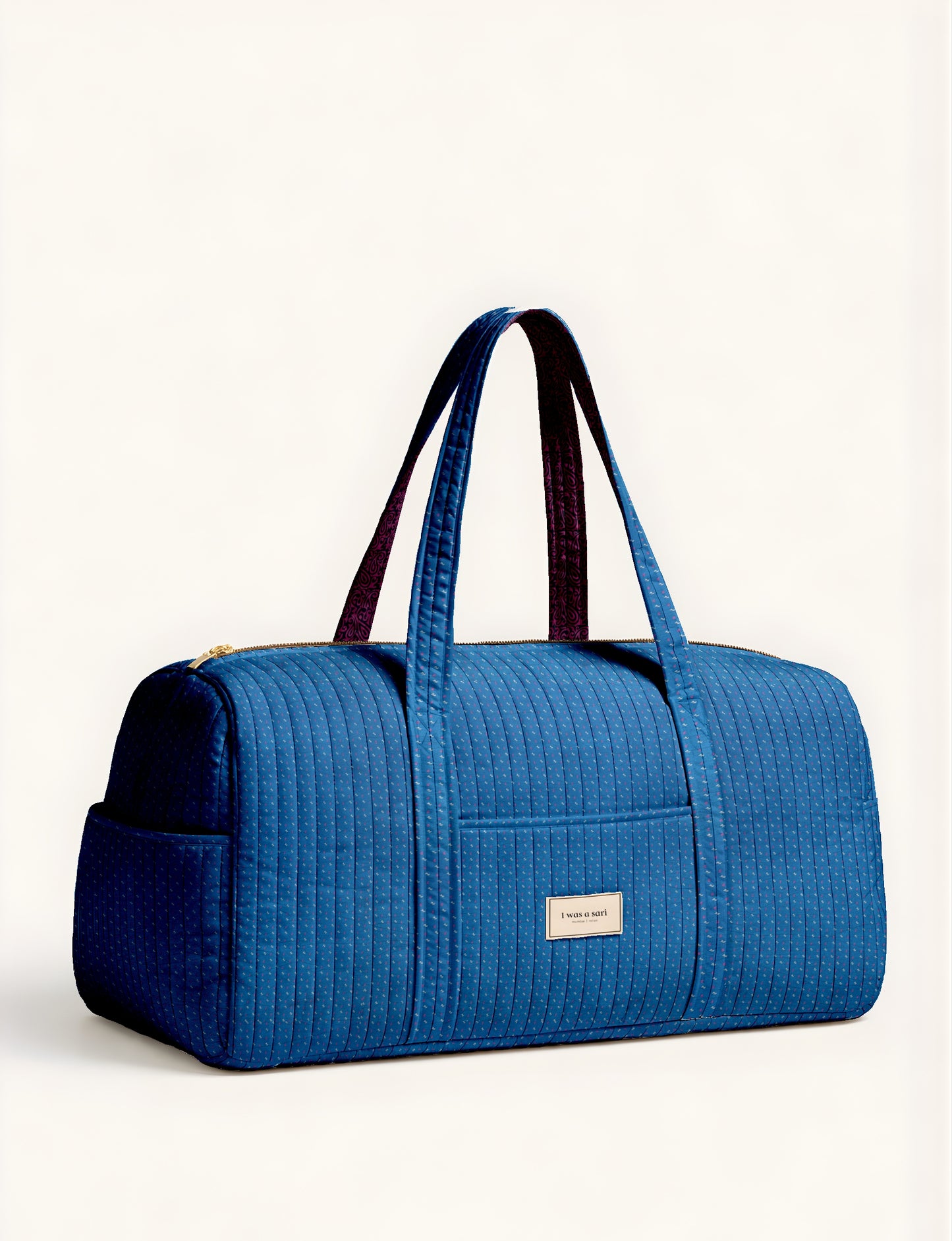 Blue quilted barrel bag with micro dot pattern, dual handles, front pocket, and gold zipper, shown in side view on white