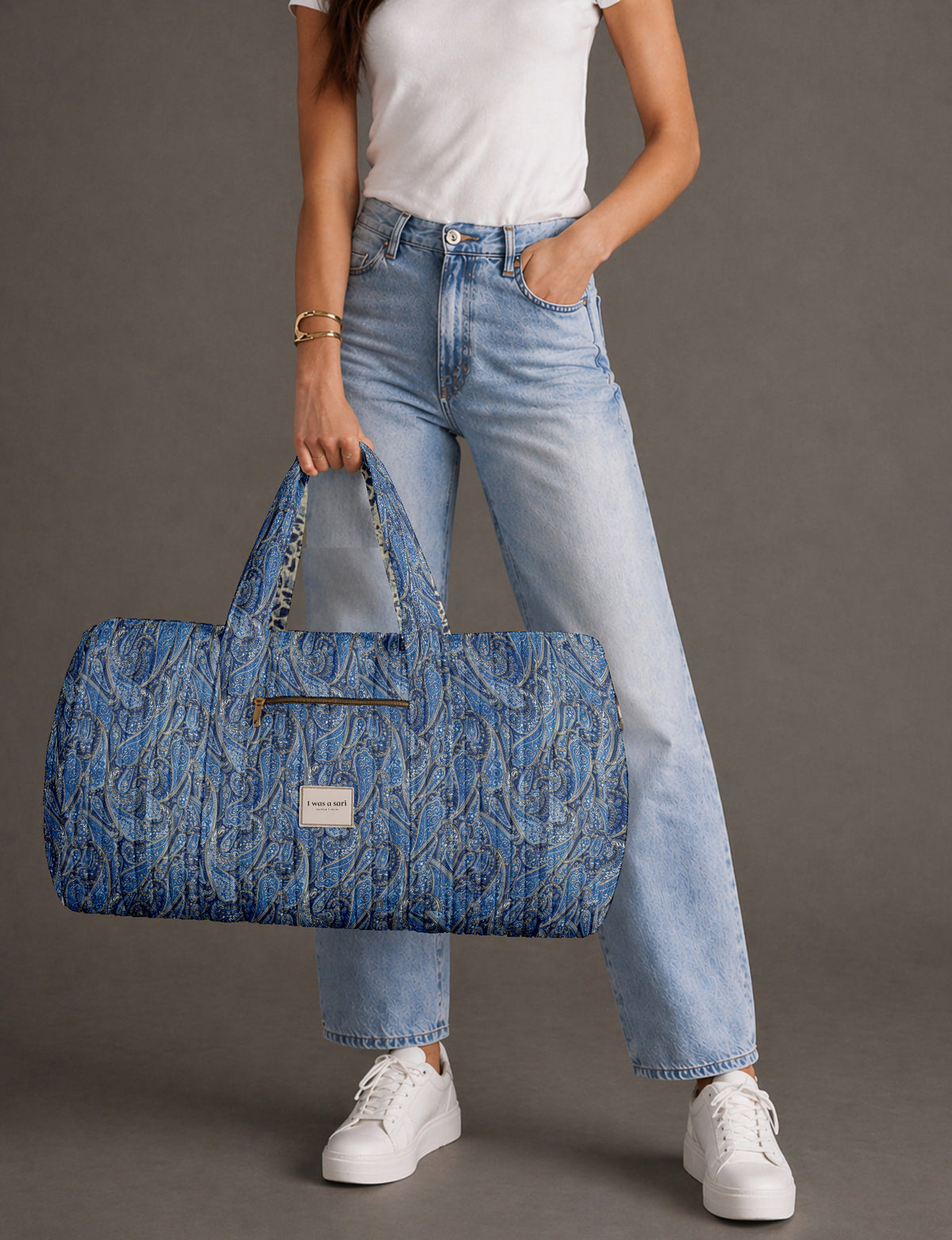 Quilted brown paisley barrel bag with double handles, front pocket, and gold zipper, shown in side angle view