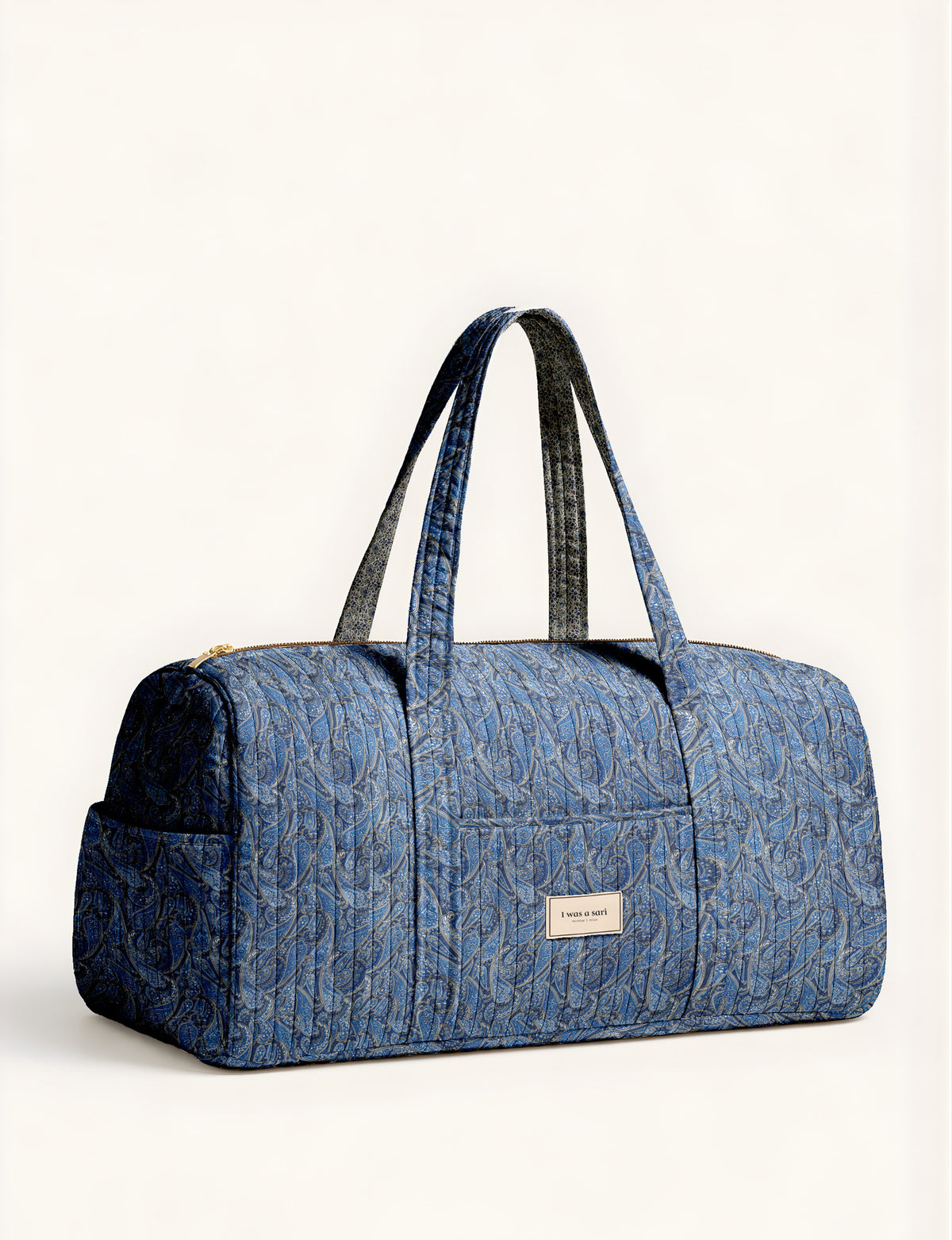 Woman holding a brown paisley quilted barrel bag with front zipper pocket, wearing light blue jeans and white sneakers
