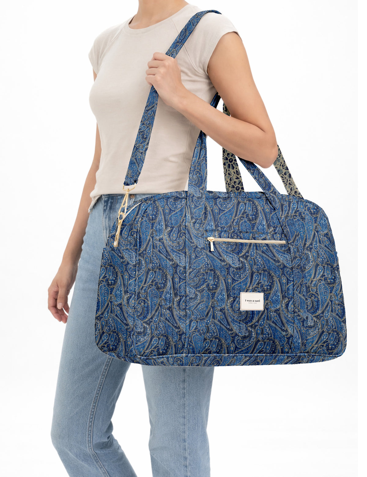 Brown quilted duffle bag with paisley pattern, front zip pocket, dual handles, and label reading "I was a sari"