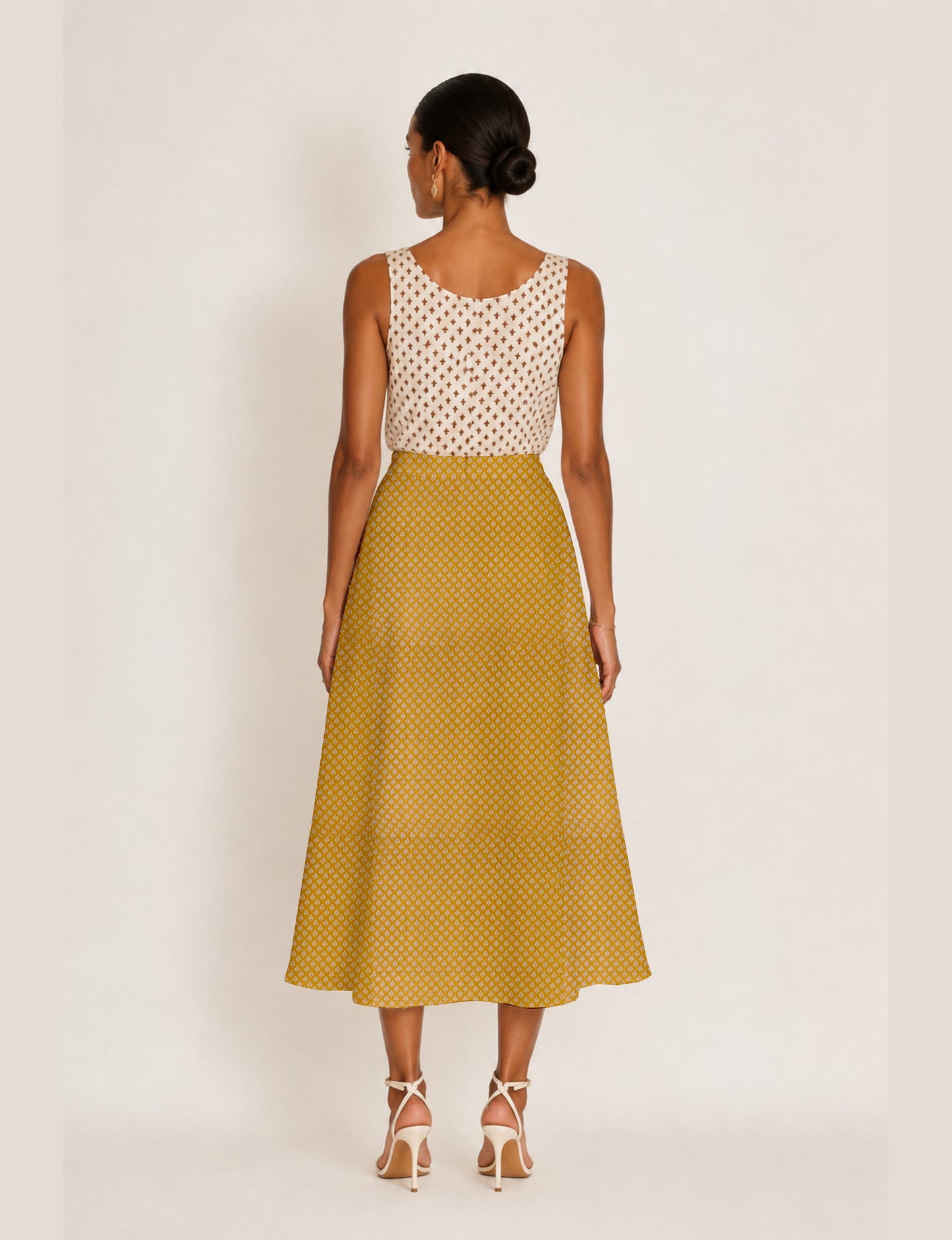 Woman wearing a yellow micro design A-line skirt with side slit, paired with a sleeveless beige top with small cross