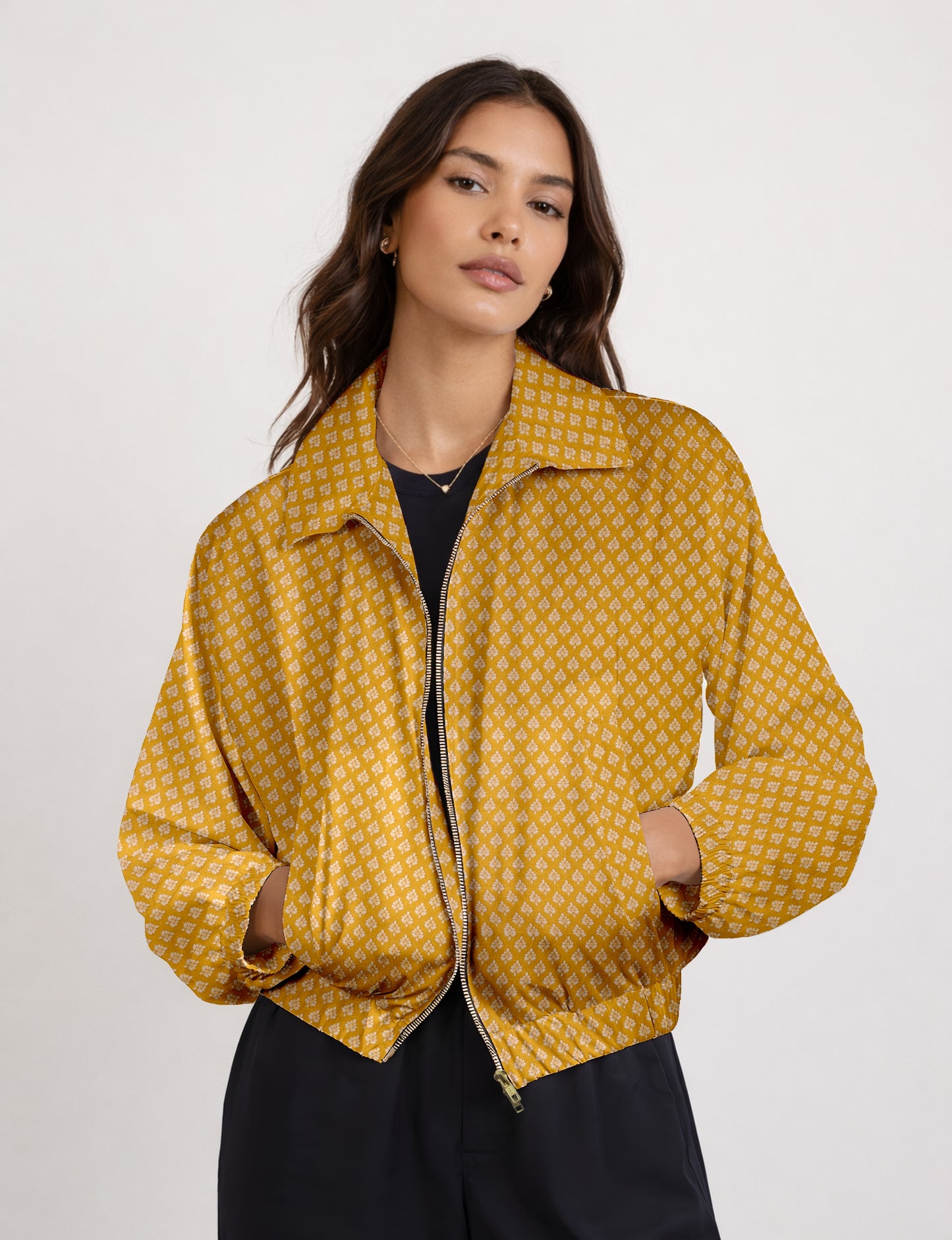 Woman wearing a yellow bomber jacket with a micro geometric pattern, front zipper, and side pockets, paired with black pants