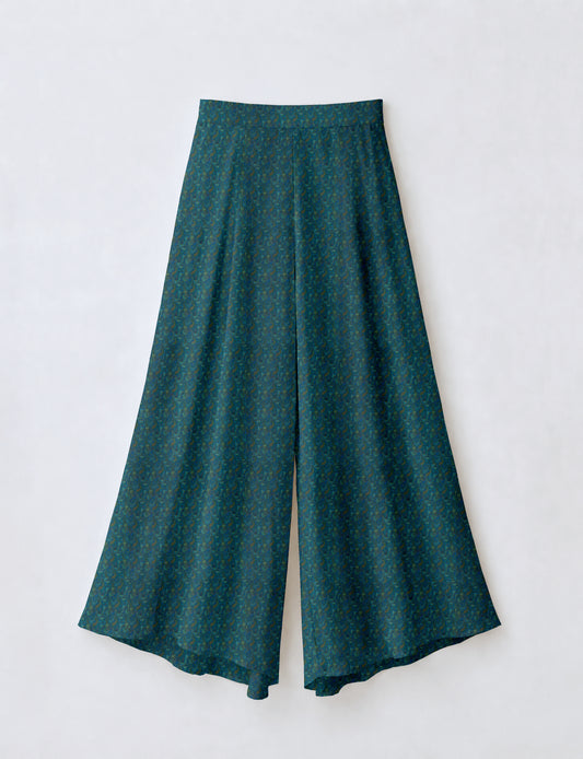 Woman wearing blue wide leg palazzo trousers with black and brown tropical floral print, side pockets, shown from back angle