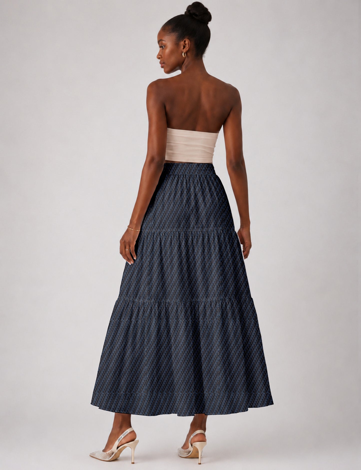 Woman wearing a yellow midi tiered skirt with a small geometric pattern, shown from the back, paired with beige top and