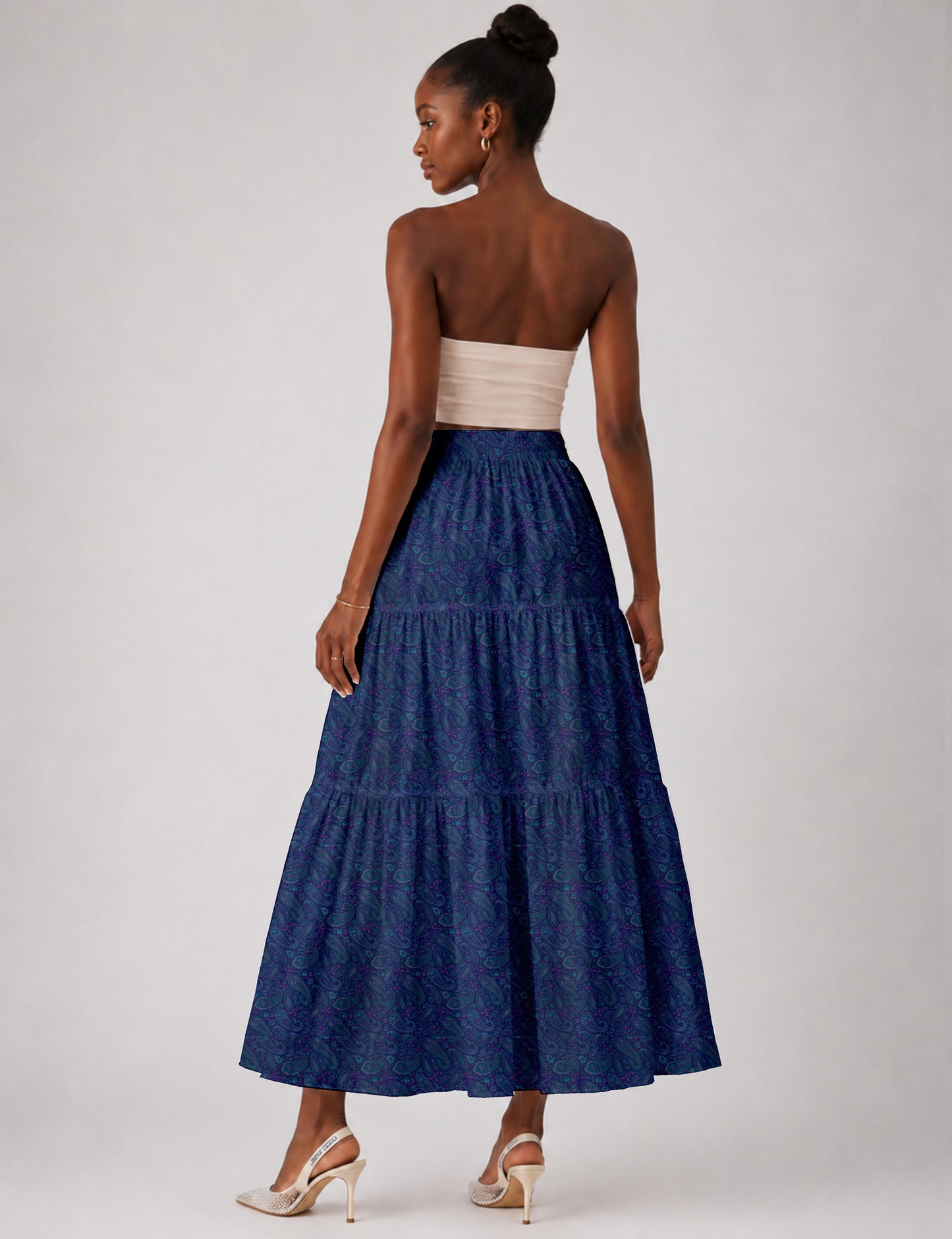Woman wearing a yellow midi tiered skirt with a small geometric pattern, paired with a beige strapless top and white heels
