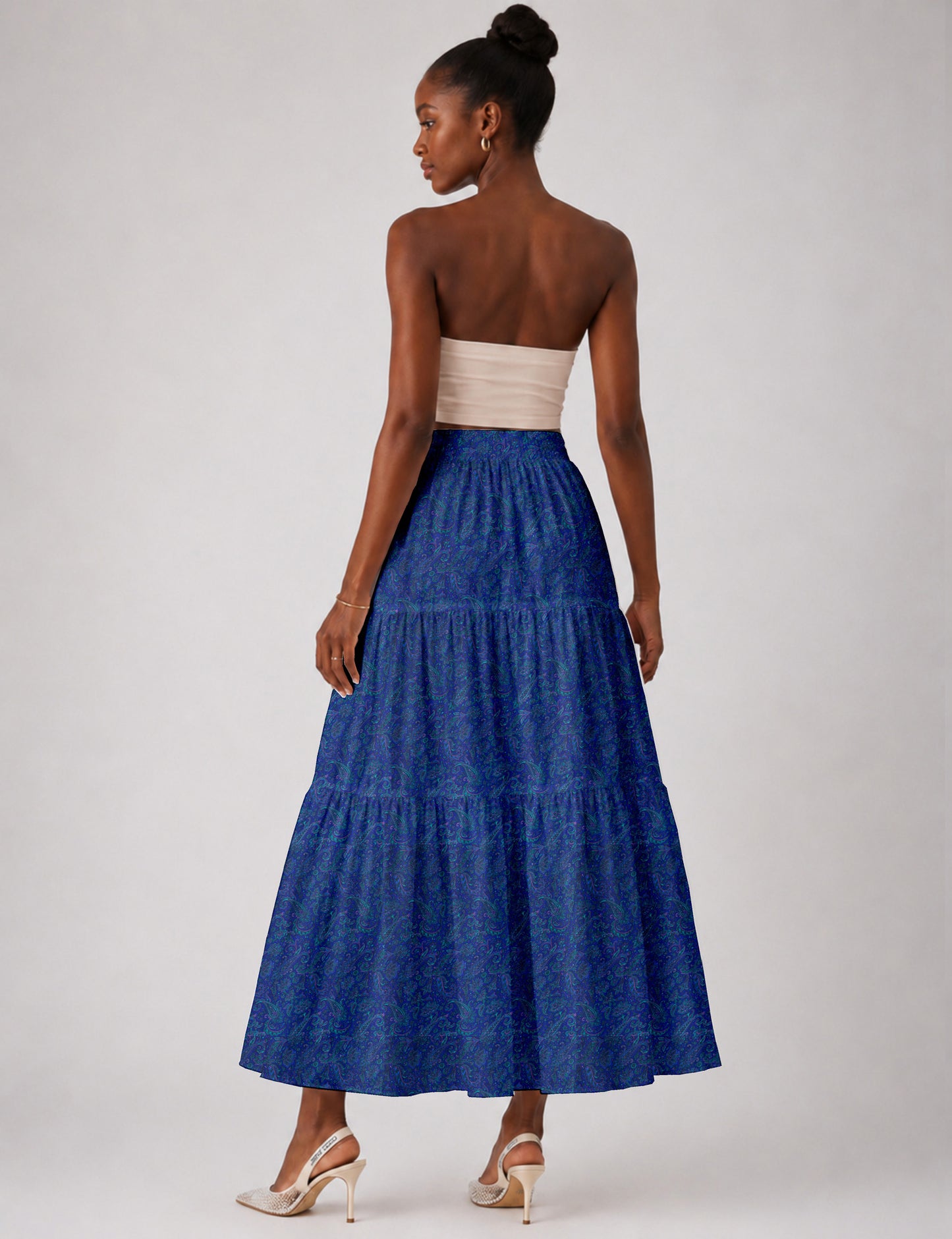 Woman wearing a yellow midi tiered skirt with a small geometric pattern, paired with a beige strapless top and white heels