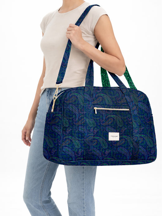 Brown quilted duffle bag with paisley pattern, front zip pocket, dual handles, and label reading "I was a sari"