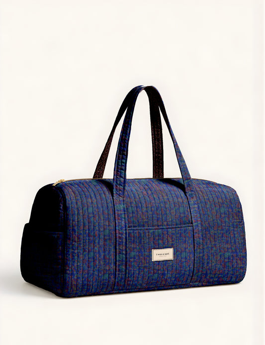 Quilted brown paisley barrel bag with double handles, front pocket, and gold zipper, shown in side angle view