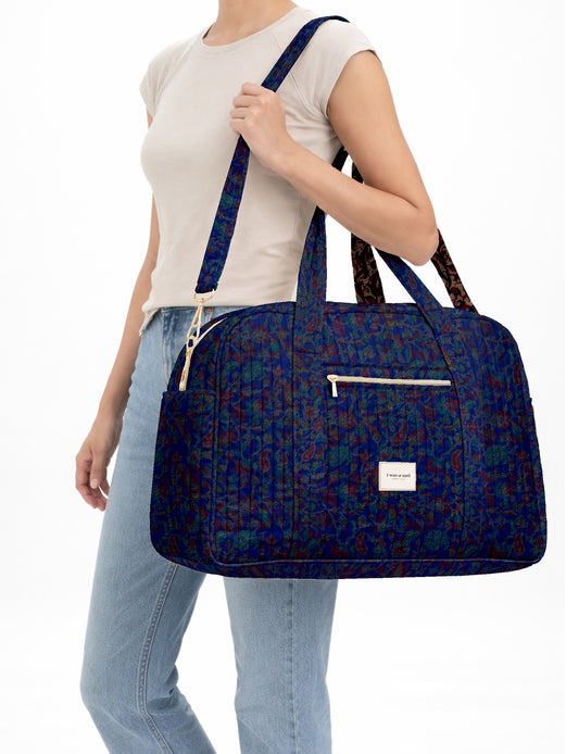 Brown quilted duffle bag with paisley pattern, front zip pocket, dual handles, and label reading "I was a sari"