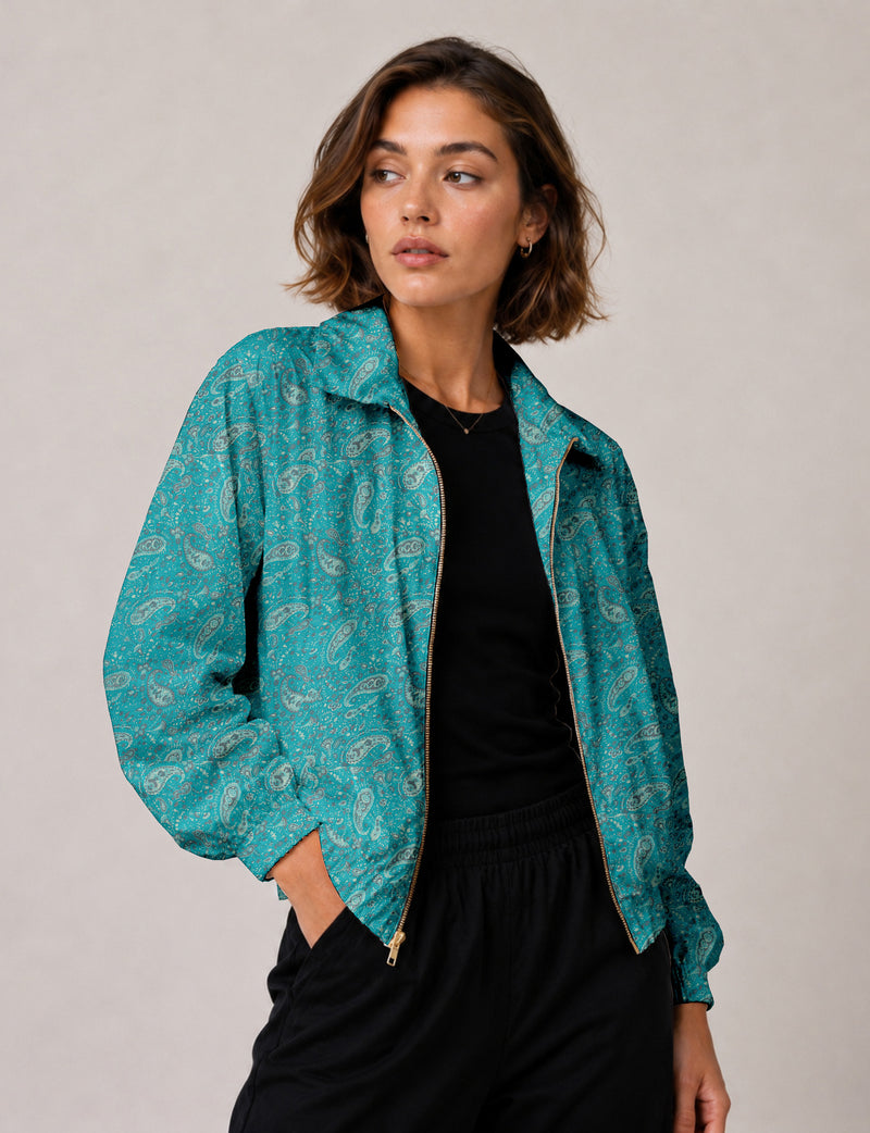 Woman wearing a blue paisley bomber jacket with a gold zipper, black top, and black pants, front view, hands in pockets