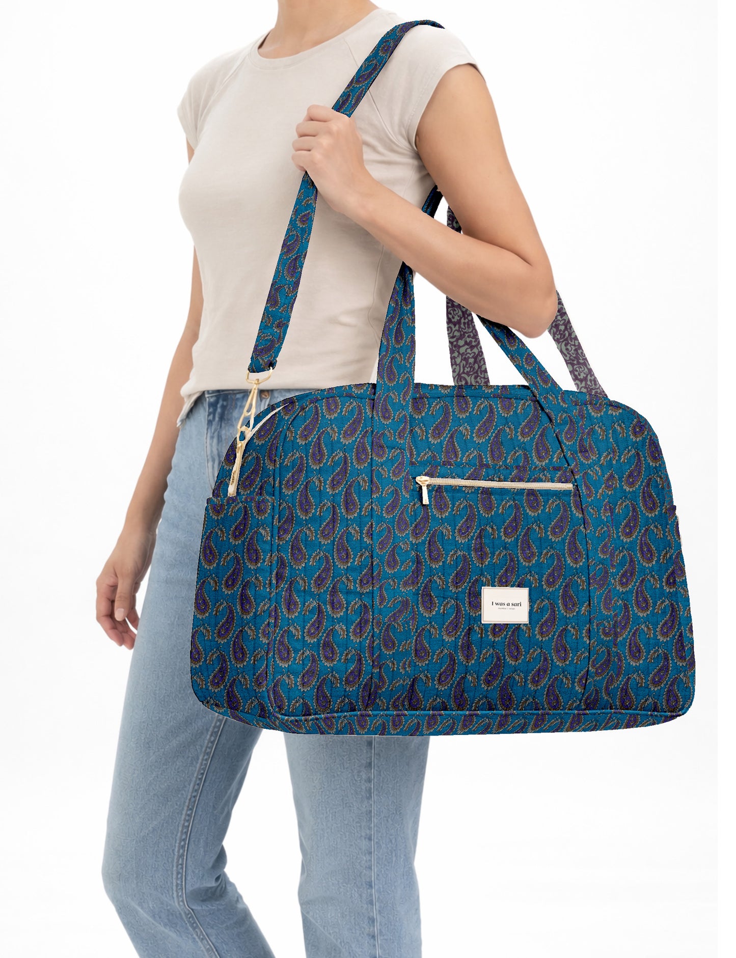 Brown quilted duffle bag with paisley pattern, front zip pocket, dual handles, and label reading "I was a sari"