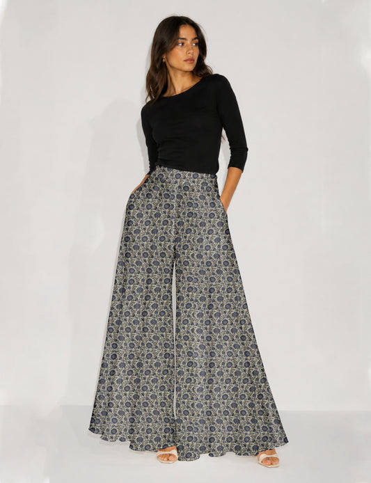 Woman wearing blue wide leg palazzo trousers with black and brown tropical floral print, side pockets, shown from back angle