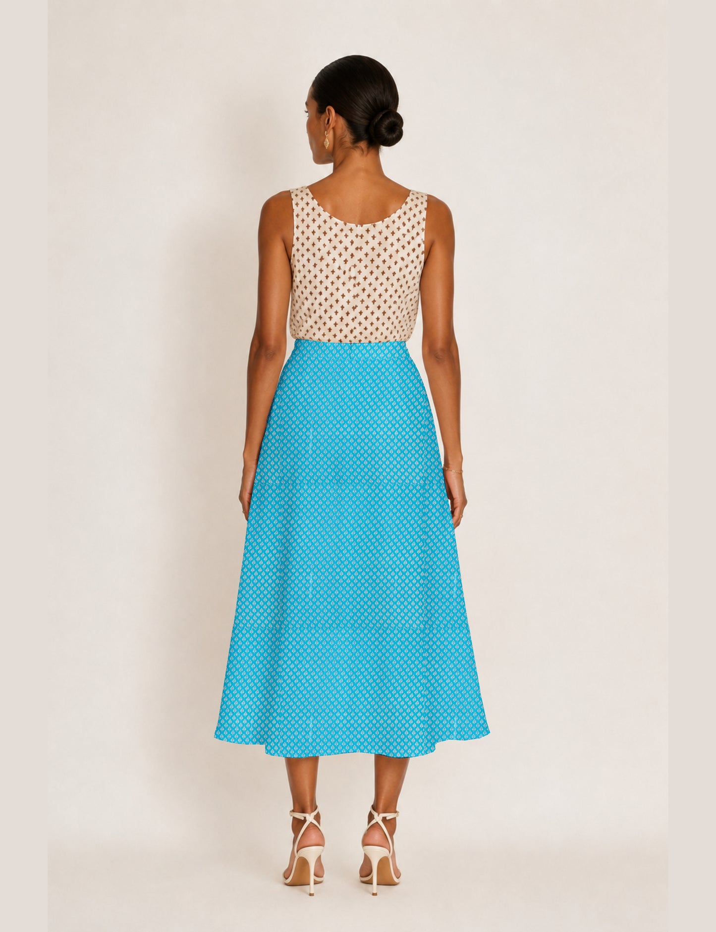 Woman wearing a yellow micro design A-line skirt with side slit, paired with a sleeveless beige top with small cross