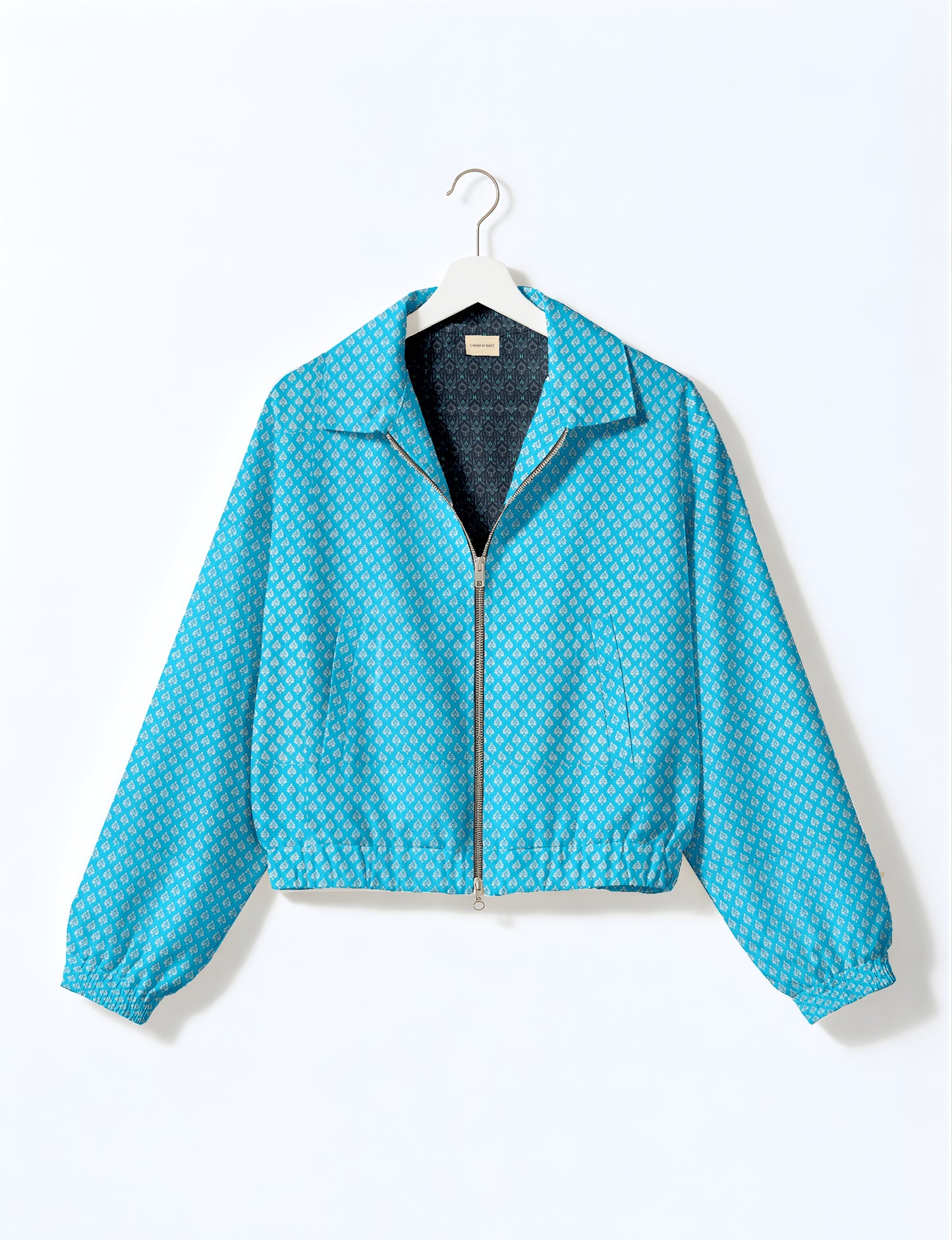Yellow bomber jacket with micro geometric pattern, silver front zipper, elastic cuffs, and blue floral inner lining, hanging