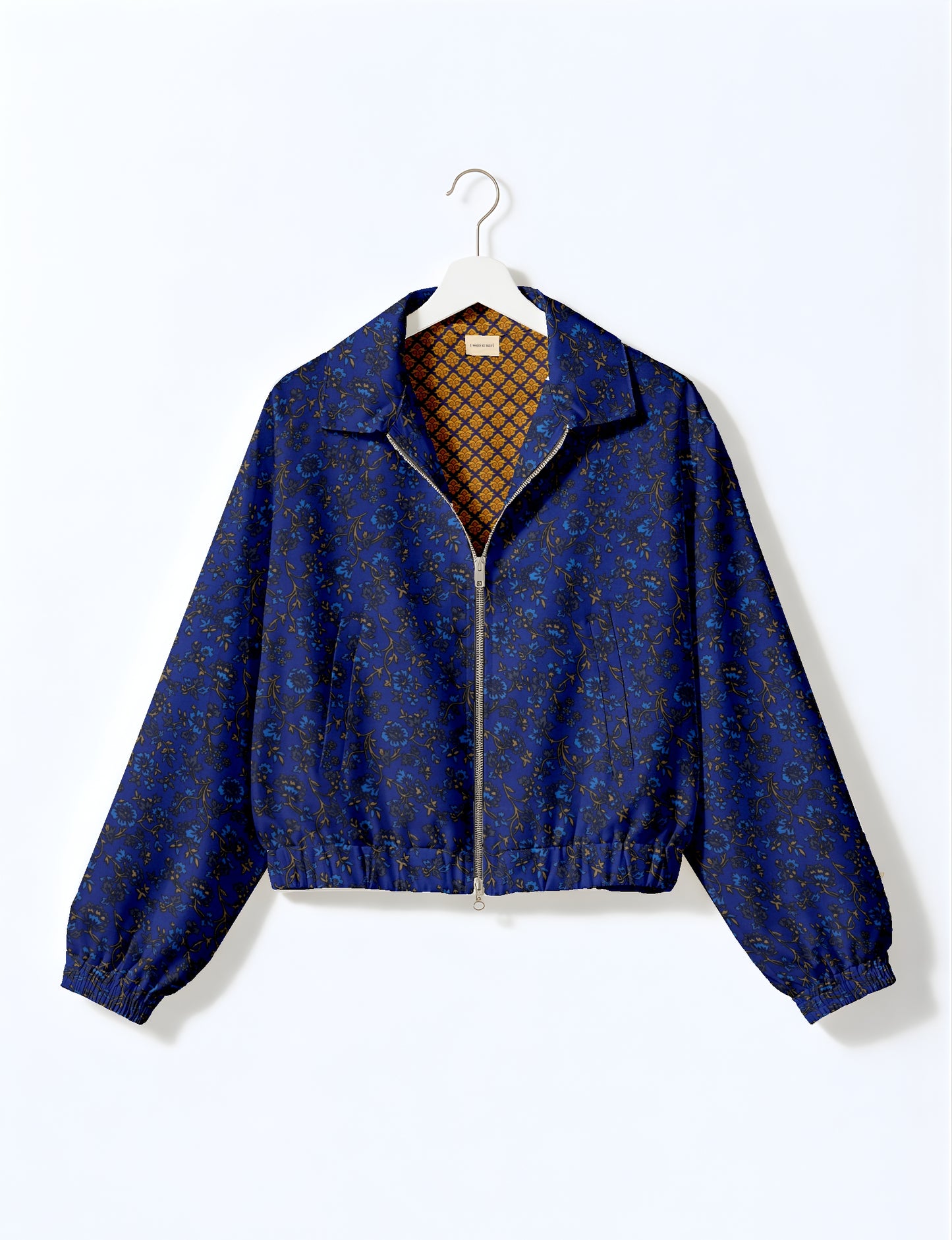 Blue bomber jacket with tropical floral print, front zipper, elastic cuffs and hem, shown on white hanger, inside patterned