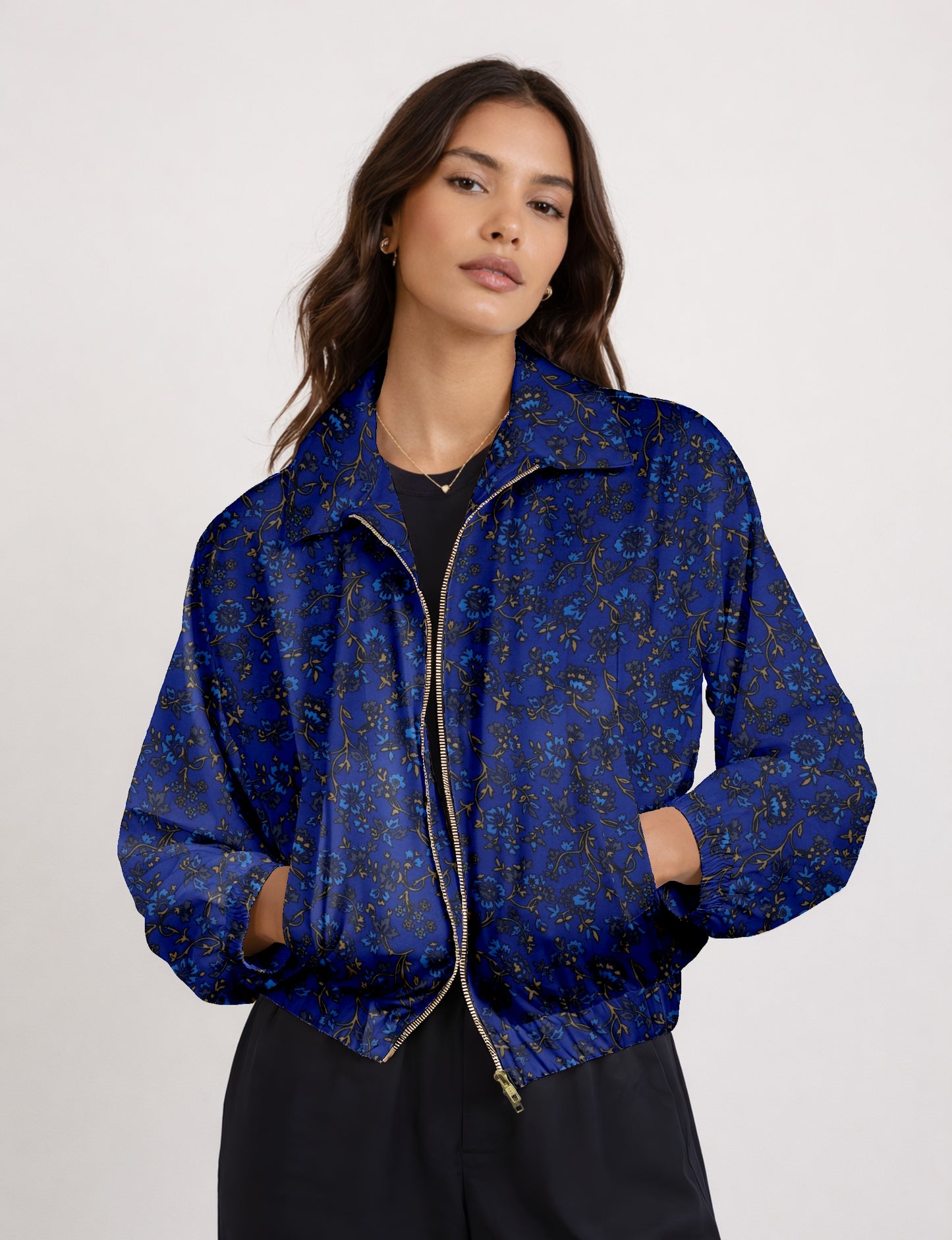 Woman wearing a blue bomber jacket with a tropical floral pattern, front zipper, elastic cuffs, and pockets, shown from