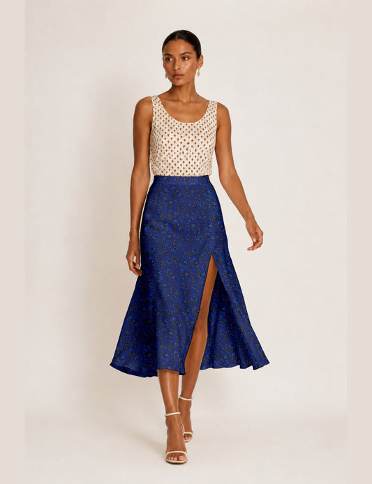 Woman wearing a blue A-line skirt with a floral tropical pattern and front slit, paired with a sleeveless beige top with