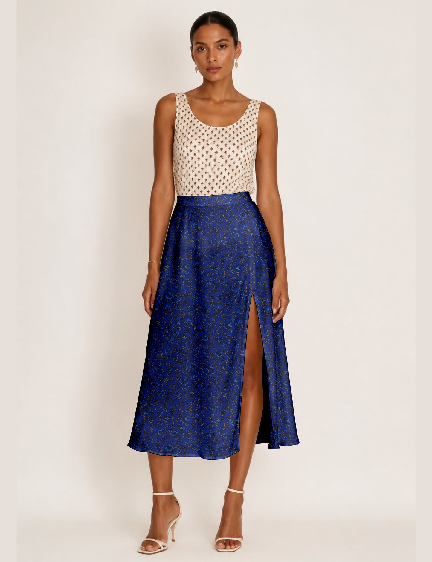 Woman wearing a blue A-line skirt with tropical floral print and front slit, paired with a sleeveless beige patterned top