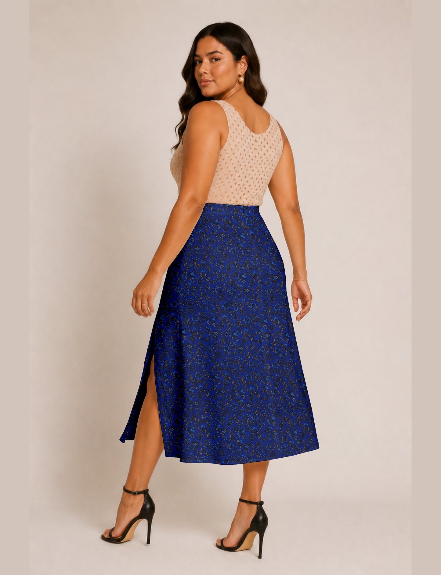 Woman wearing a blue tropical A-line skirt with side slit, paired with a beige sleeveless top, shown from back angle