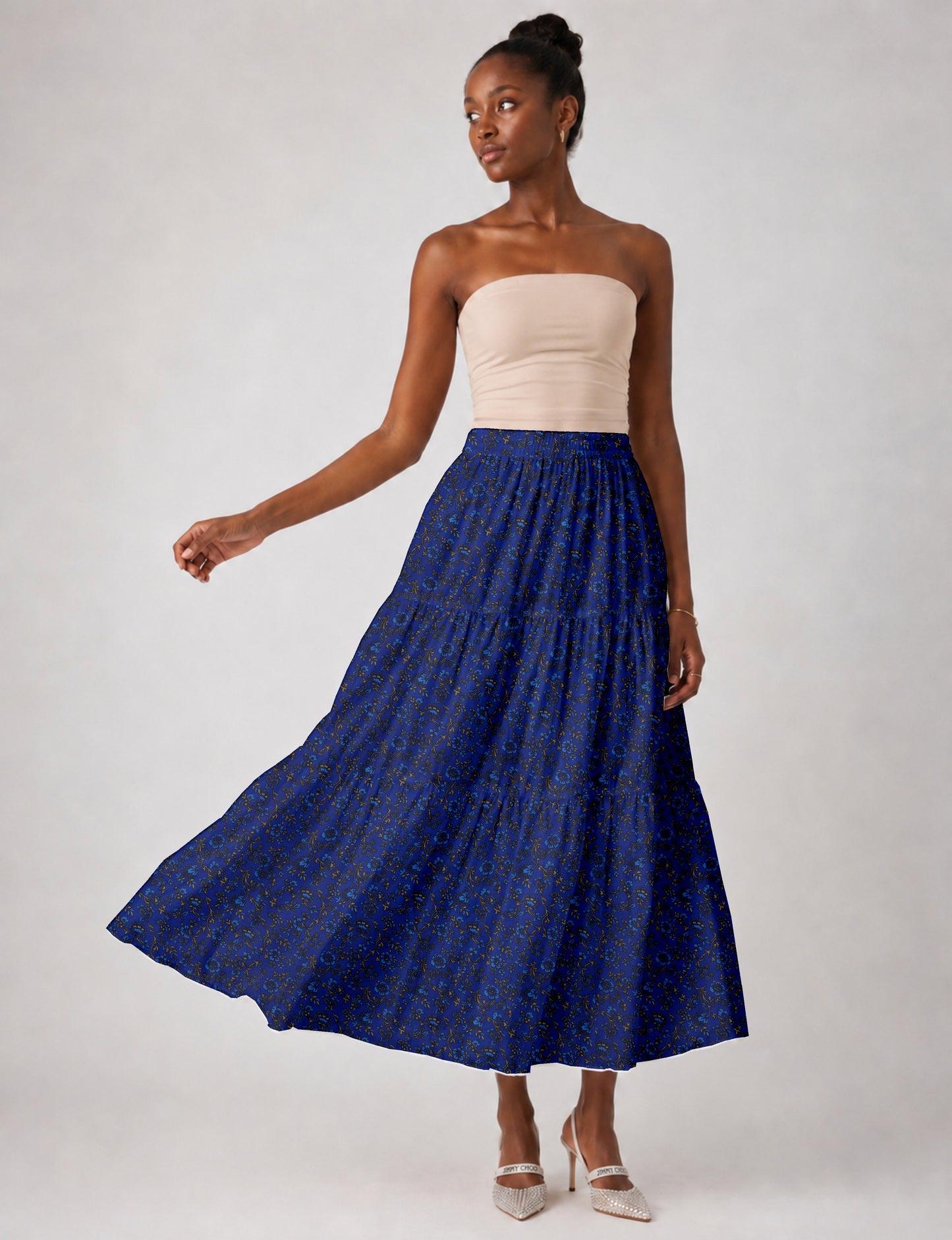 Woman wearing a blue tropical print midi tiered skirt with a beige strapless top and white pointed heels