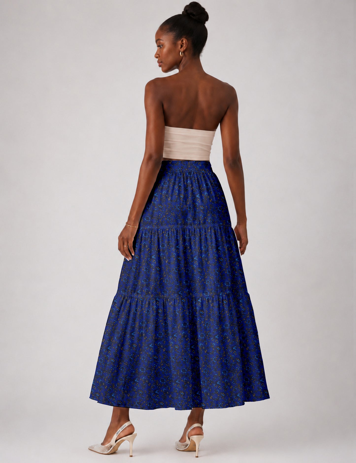 Woman wearing a blue tropical print midi tiered skirt, back view, paired with beige strapless top and beige high heels