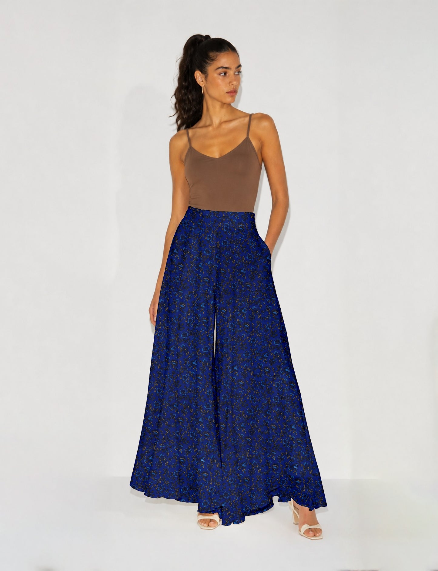 Woman wearing blue wide leg palazzo trousers with black and brown floral print, paired with brown sleeveless top and white
