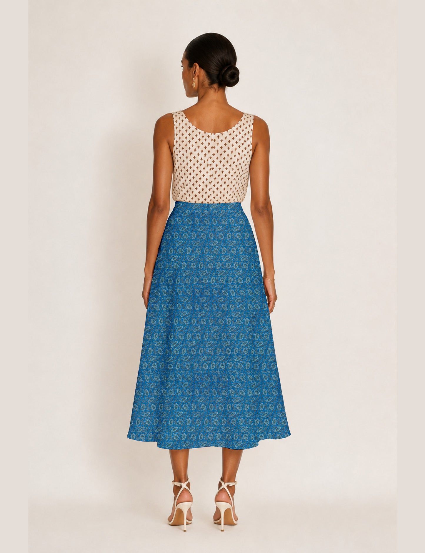 Woman wearing a yellow and black micro patterned A-line skirt with front slit, paired with beige sleeveless top and black
