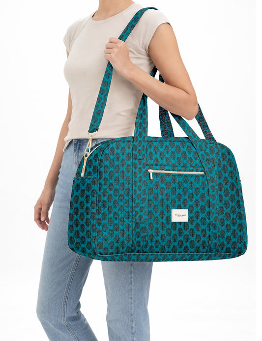 Brown quilted duffle bag with paisley pattern, front zip pocket, dual handles, and label reading "I was a sari"