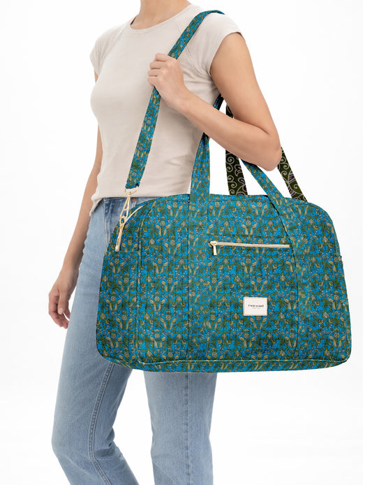 Brown quilted duffle bag with paisley pattern, front zip pocket, dual handles, and label reading "I was a sari"