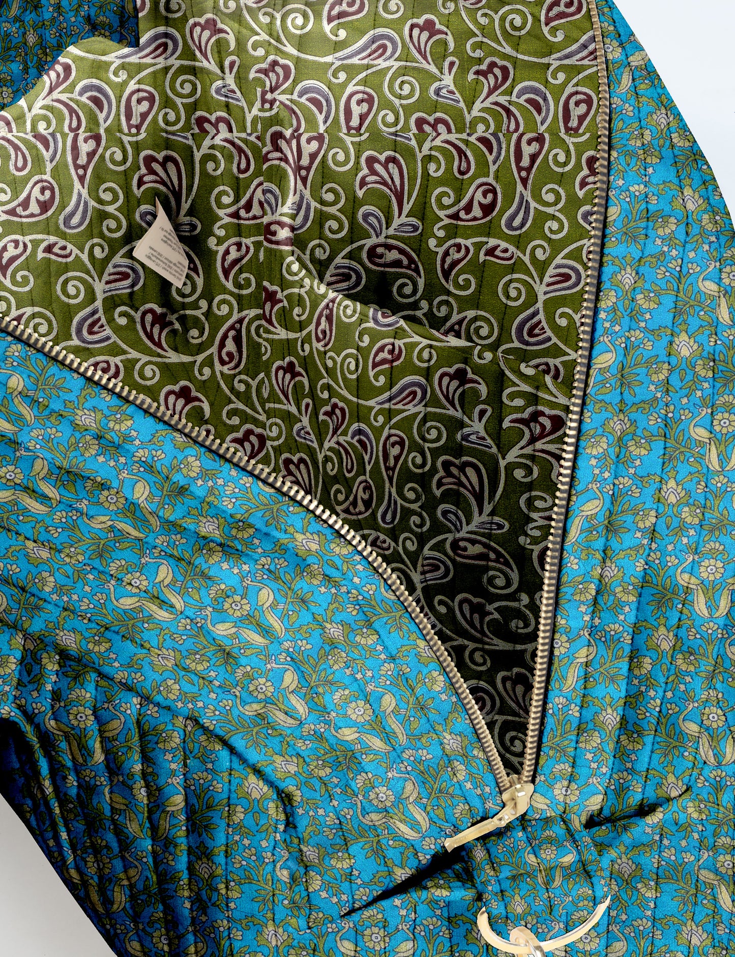 Brown quilted duffle bag with paisley pattern, front zip pocket, dual handles, and label reading "I was a sari"
