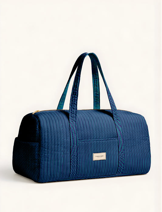 Quilted brown paisley barrel bag with double handles, front pocket, and gold zipper, shown in side angle view