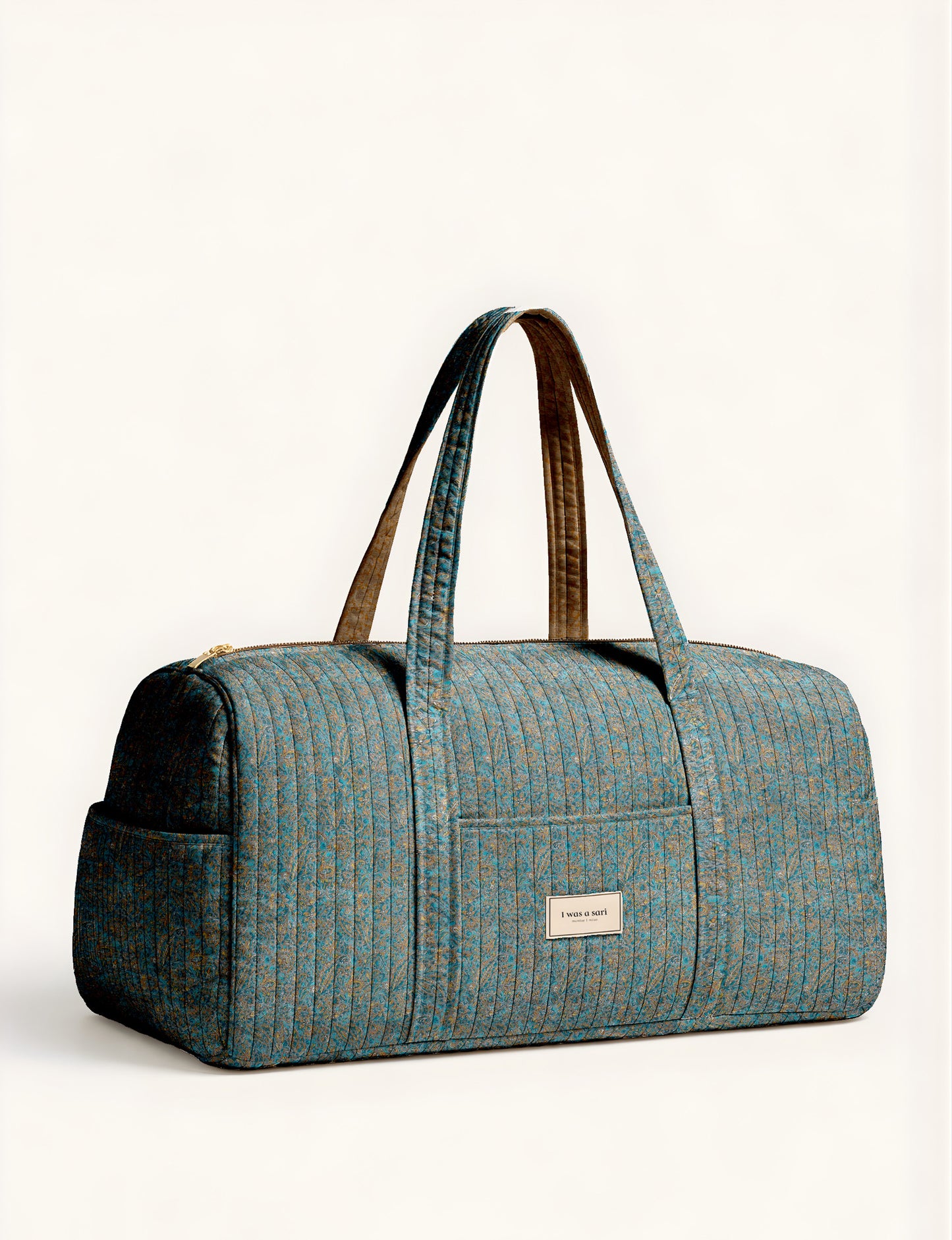 Quilted brown paisley barrel bag with double handles, front pocket, and gold zipper, shown in side angle view