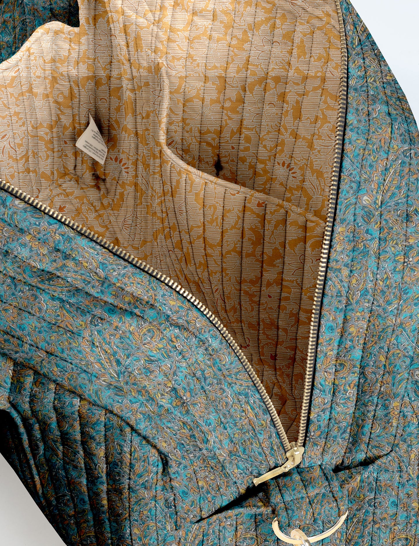Brown quilted duffle bag with paisley pattern, front zip pocket, dual handles, and label reading "I was a sari"