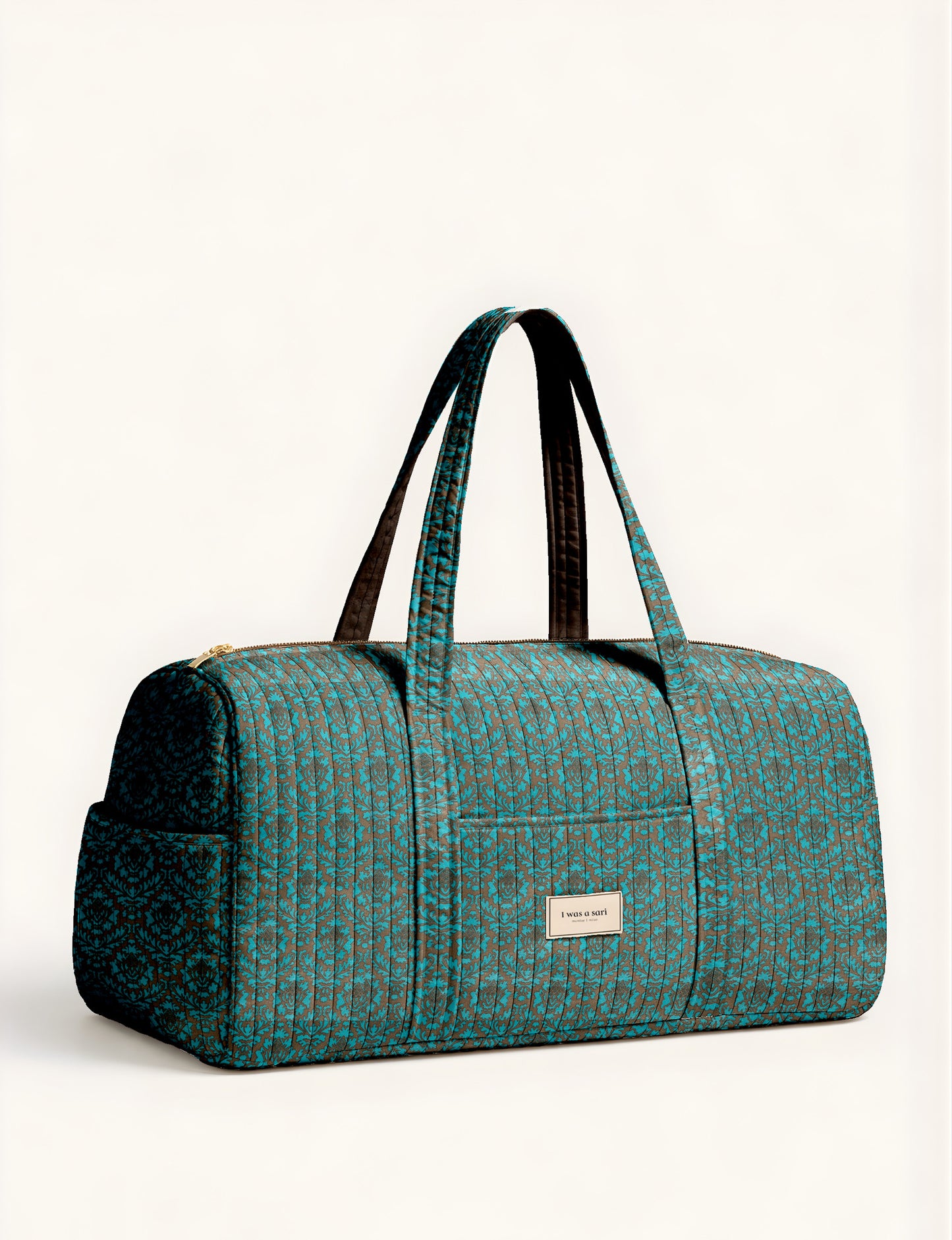 Quilted brown paisley barrel bag with double handles, front pocket, and gold zipper, shown in side angle view