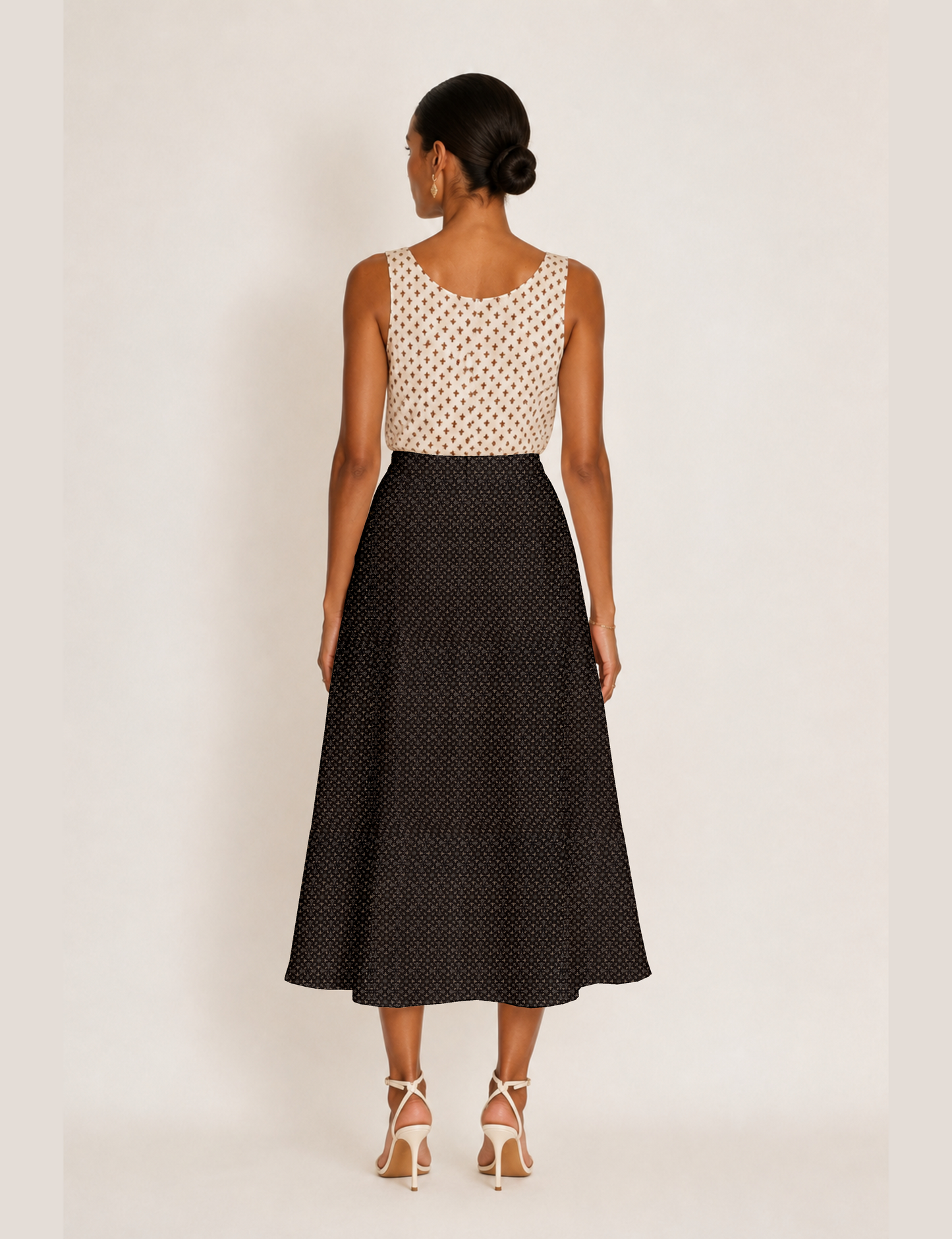Woman wearing a yellow and black micro patterned A-line skirt with front slit, paired with beige sleeveless top and black