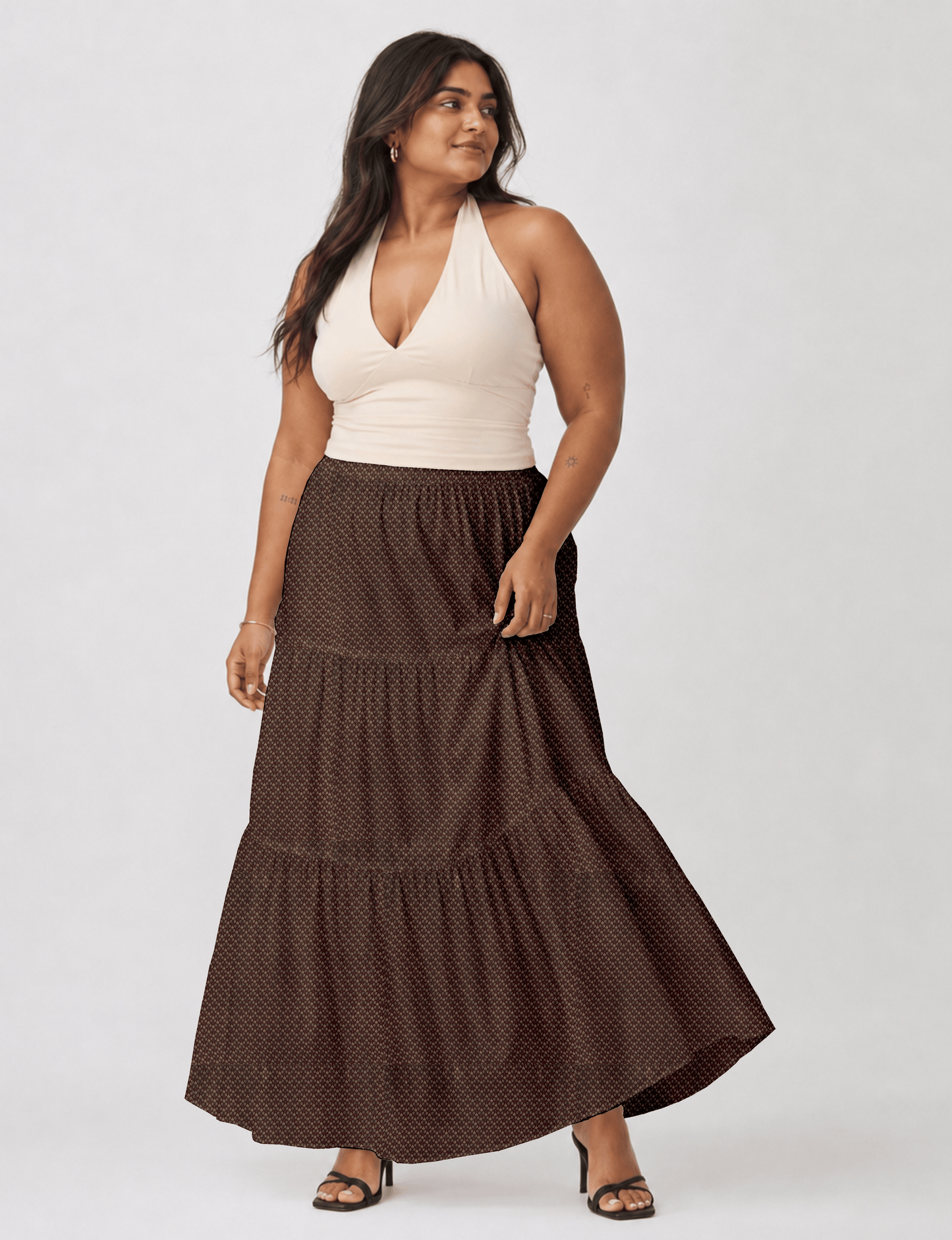 Woman wearing a yellow midi tiered skirt with a small geometric pattern, paired with a beige strapless top and white heels