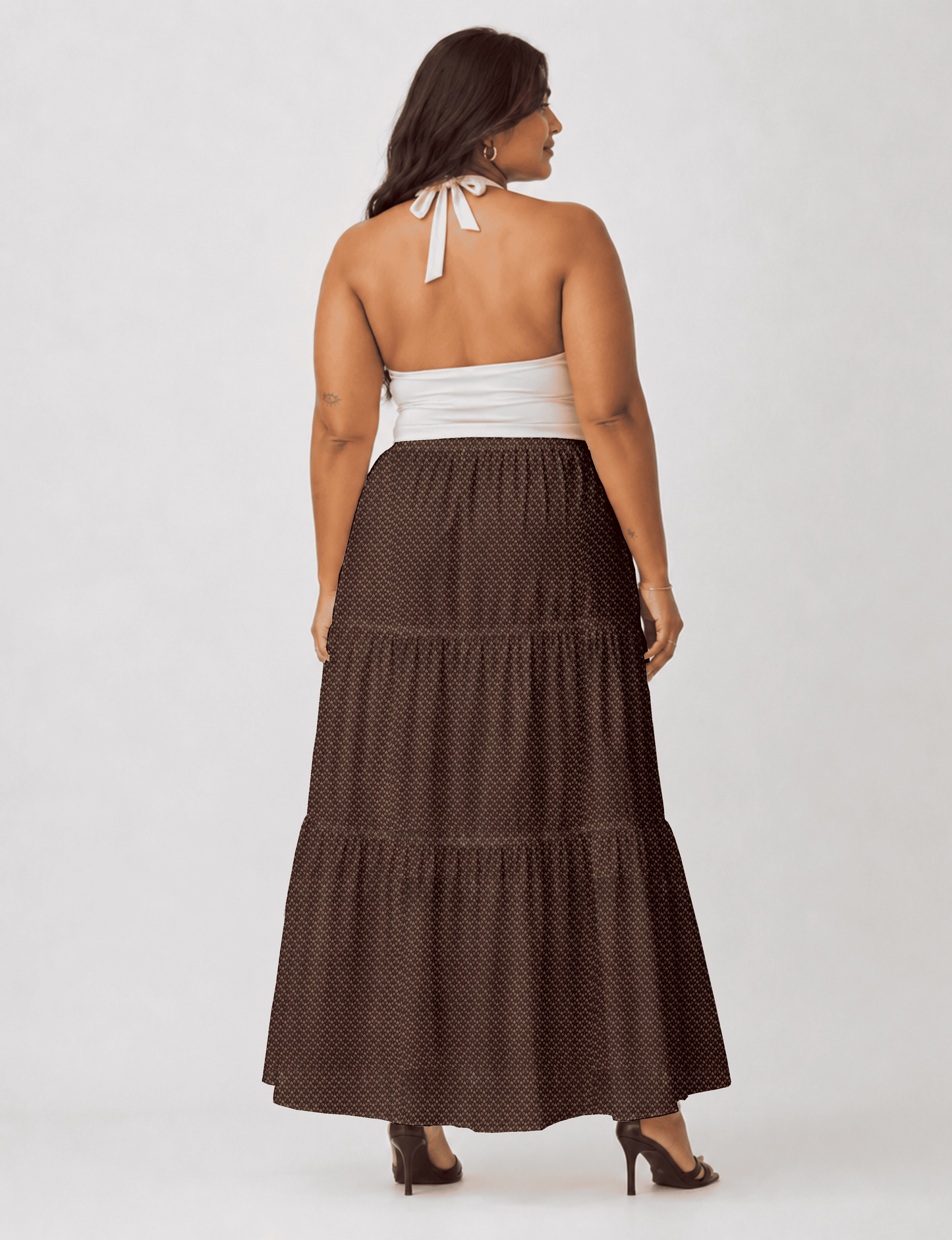 Woman wearing a yellow midi tiered skirt with a small geometric pattern, shown from the back, paired with beige top and