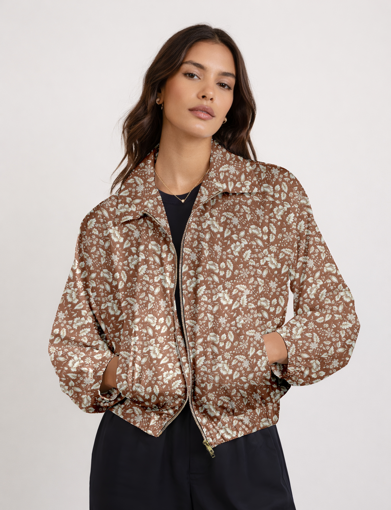 Woman wearing brown floral bomber jacket with front zipper and side pockets, paired with black pants, front view