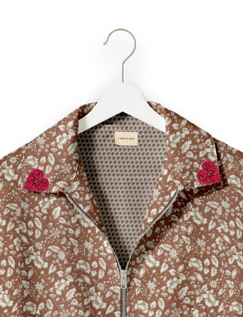 Brown floral bomber jacket with front zipper, pink beaded heart patches on collar, and "I was a sari" label inside collar