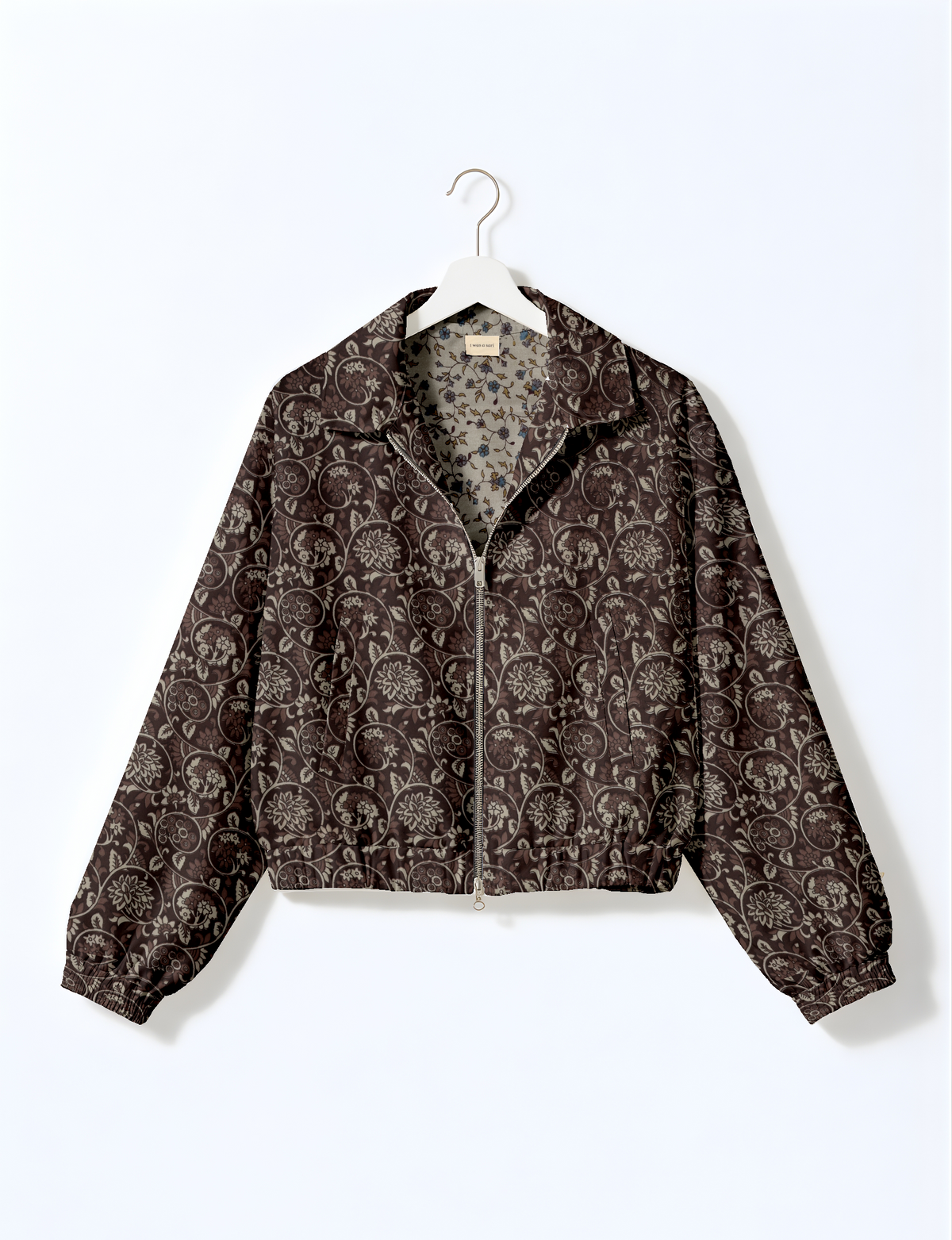 Brown floral bomber jacket with zipper front and elastic cuffs hanging on white hanger against white background