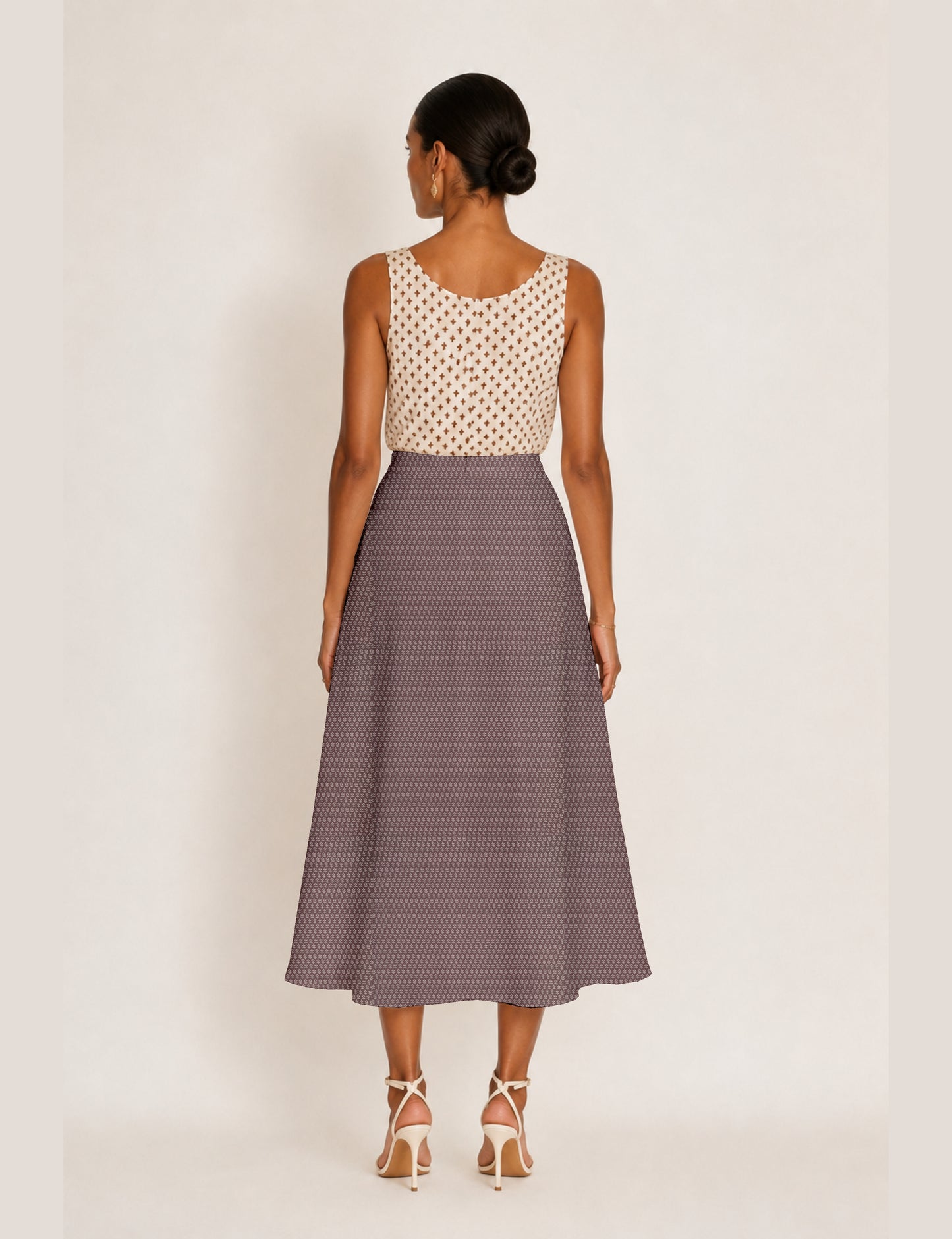Woman wearing a yellow micro design A-line skirt with side slit, paired with a sleeveless beige top with small cross