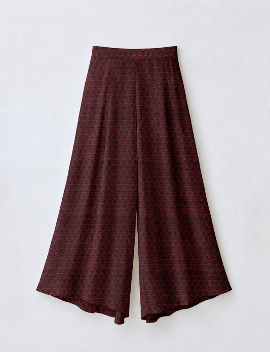 Woman wearing blue wide leg palazzo trousers with black and brown tropical floral print, side pockets, shown from back angle