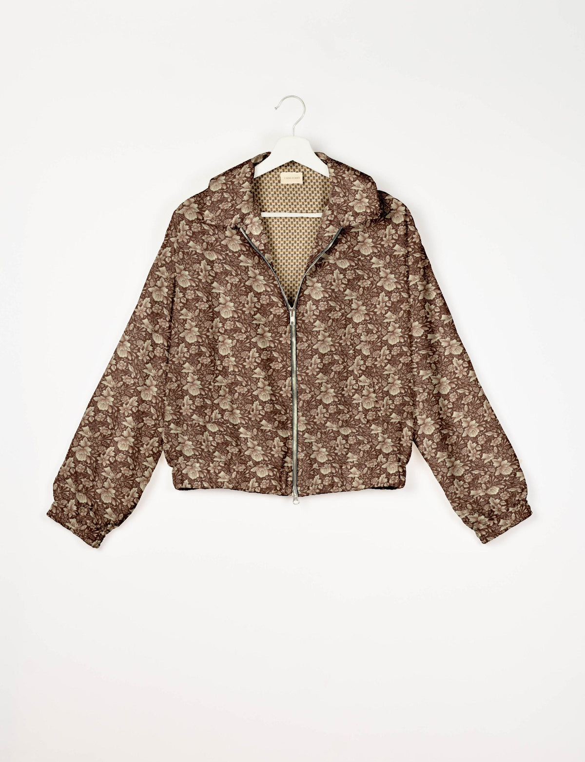 Brown bomber jacket with tropical floral pattern, front zipper, elastic cuffs, and contrasting small geometric print lining