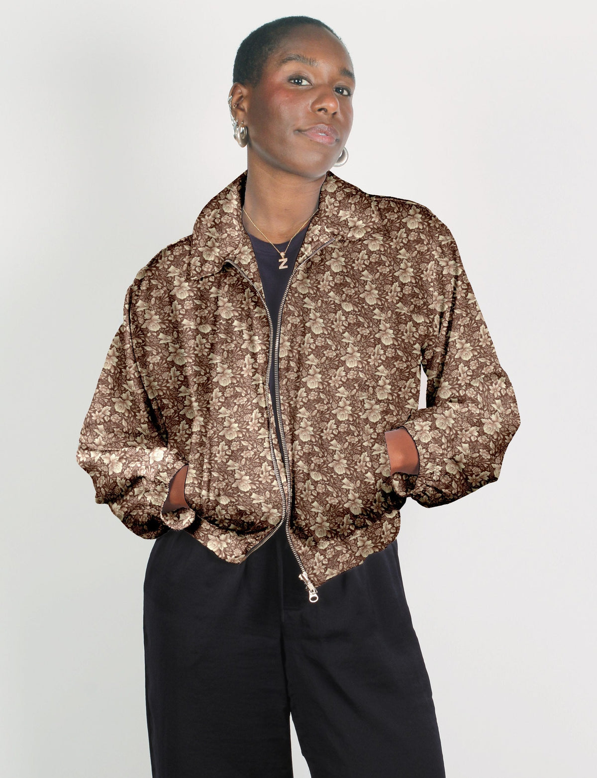 Woman wearing a brown bomber jacket with beige tropical floral print, front zipper, and side pockets, paired with black