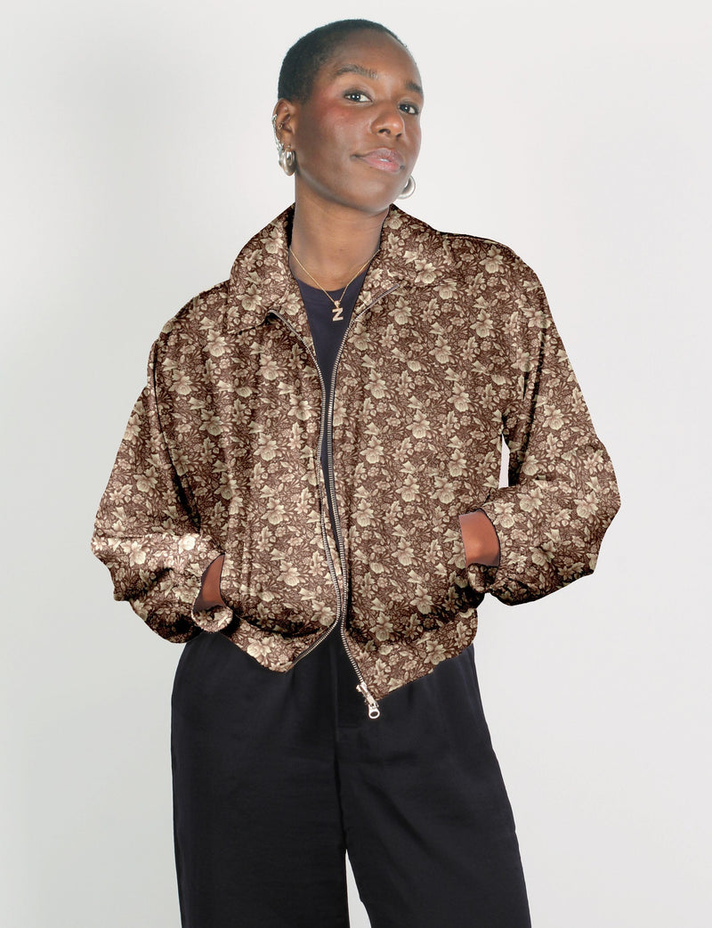 Woman wearing a brown bomber jacket with beige tropical floral print, front zipper, and side pockets, paired with black