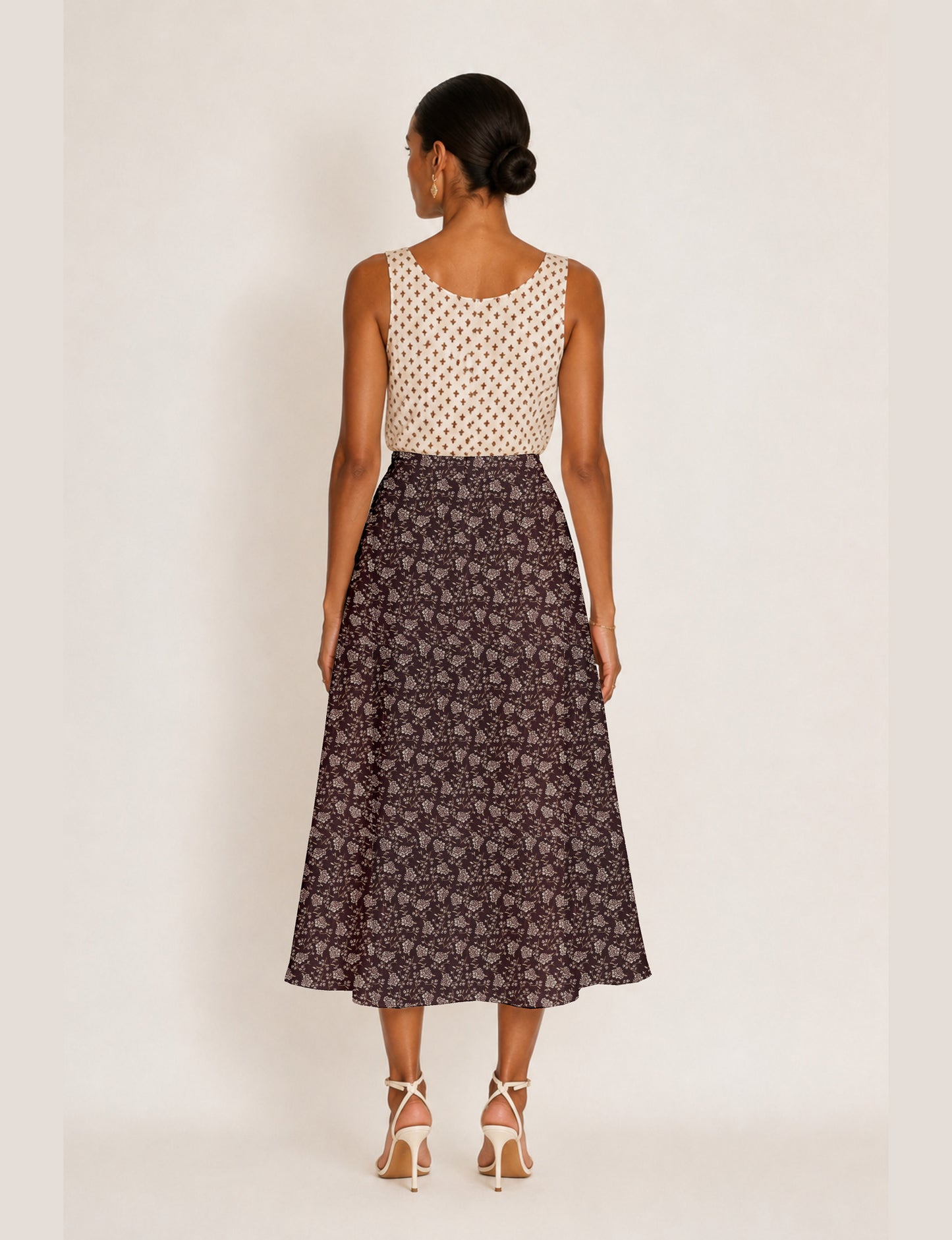 Woman wearing a yellow and black micro patterned A-line skirt with front slit, paired with beige sleeveless top and black