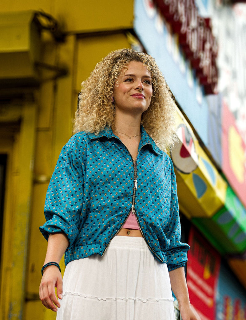 Woman wearing a blue zip-up jacket with small floral print and rolled sleeves, paired with a white skirt, front view