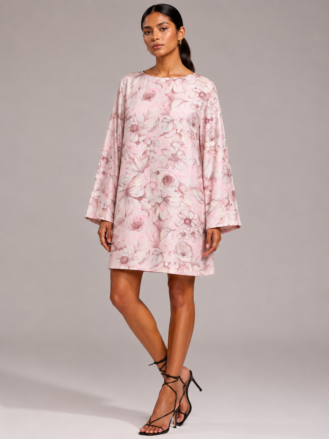 Woman wearing a pink floral swing dress with long wide sleeves and a round neckline, paired with black strappy heels
